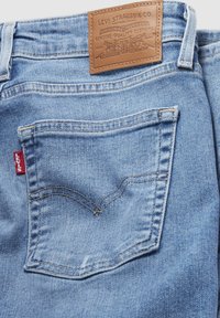Jeans de denim azul claro con un parche de cuero marrón etiquetado "Levi Strauss & Co." y una etiqueta roja en el costado; presenta un bolsillo trasero con detalles de costura.