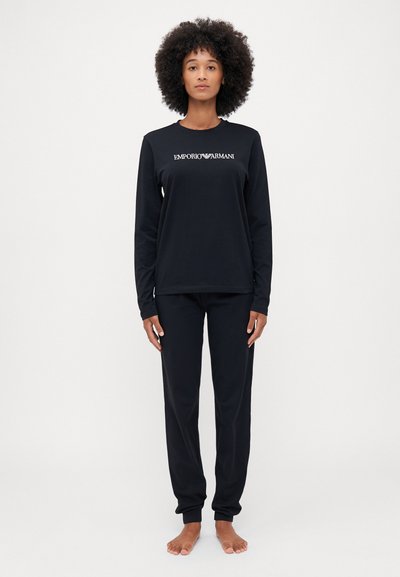 Haut noir à manches longues avec le logo "EMPORIO ARMANI" ; pantalon noir assorti. Les deux sont fabriqués dans un tissu doux et lisse avec une coupe décontractée.
