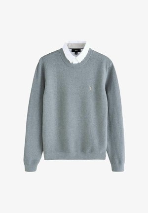 Pull en mailles texturé gris clair porté par-dessus une chemise blanche avec col, des manches longues, encolure ronde avec un petit logo brodé sur la poitrine.