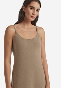 Beige stickad klänning med tunna band, rundad halsringning, mjuk textur, åtsittande silhuett och subtila detaljfinishar. Enkelt och elegant design.
