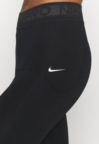 Czarne legginsy sportowe z szerokim, teksturowanym pasem w talii, na którym znajduje się branding "PRO" oraz "NIKE". Minimalistyczne logo Nike w kolorze białym po boku.