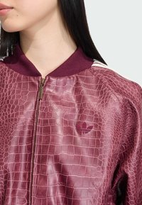 Bordo bomber jakna s reljefnim uzorkom krokodila, rebrastim ovratnikom i diskretnim izvezenim logom na prsima. Vidljivo zatvaranje na zip.