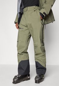 Pantaloni de schi în verde măsliniu cu accente negre. Au un talie înaltă, un talie ajustabilă, multiple buzunare și un finisaj rezistent la apă.