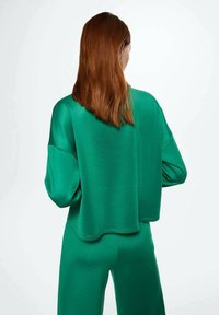 Zielony, oversize'owy sweter o gładkiej fakturze, z opadającymi ramionami i zaokrąglonym dołem, w połączeniu z dopasowanymi spodniami.