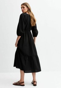 Black, long-sleeve dress with a gathered waist and tiered hem. Soft fabric with a smooth texture, featuring a classic design.