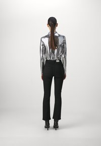 Stříbrný top s flitry a dlouhým rukávem spárovaný s černými rozšiřujícími se kalhotami a kotníkovými botami. Oblečení má přiléhavý střih a lesklou texturu.