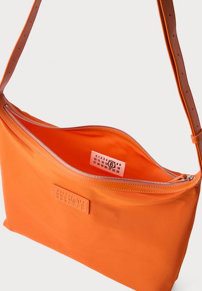 Πορτοκαλί τσάντα crossbody με ρυθμιζόμενο λουρί, άνοιγμα με φερμουάρ και ετικέτα που έχει αριθμούς και έναν κύκλο γύρω από το έξι μπροστά και εσωτερικά.