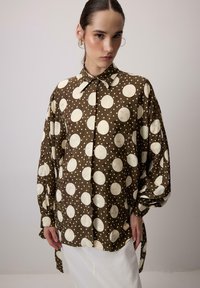 Camicia button-up a pois marroni con grandi cerchi crema e piccoli pois bianchi. Presenta un colletto classico e una vestibilità ampia con maniche lunghe.