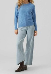 Blå texturerad tröja med långa ärmar, kombinerad med ljusblå vida jeans och bruna ankelboots. Enkel design utan mönster.