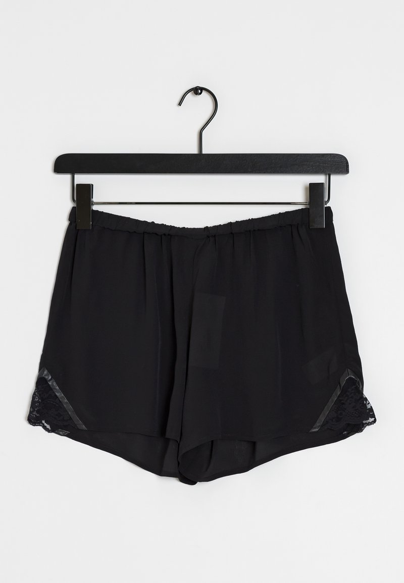 Shorts noirs amples avec taille élastique et bordure en dentelle sur les côtés, suspendus à un cintre à pinces noir sur fond blanc.