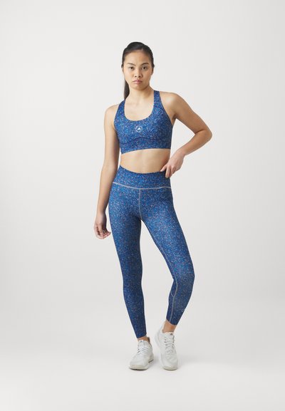 Top corto atlético azul y leggings de cintura alta con un patrón floral, hechos de un tejido elástico, combinados con zapatillas deportivas blancas.