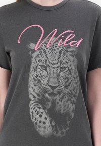 Grijze t-shirt met een grote luipaardafbeelding in grijstinten, met het woord "Wild" in roze cursief boven de afbeelding.