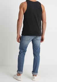 Canotta nera in cotone senza maniche, jeans azzurri a gamba affusolata con risvolti, e sneakers bianche. Design semplice con una vestibilità classica.