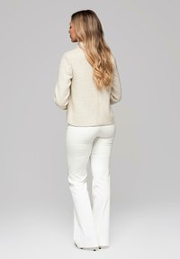 Kremowa teksturowana kurtka z kołnierzem, zestawiona z białymi rozszerzanymi spodniami. Kurtka ma pleciony wzór i prosty krój.