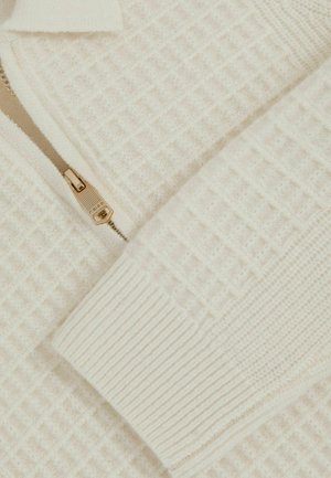 Krēmkrāsas zip-up džemperis ar teksturētu vafeļu rakstu, ar ribu aprocēm un metāla rāvējslēdzēju ar zelta apdari.