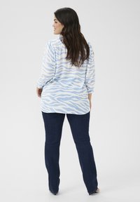 Light blue long-sleeve blouse with white wave pattern, paired with dark blue jeans. Soft, textured fabric with a loose fit.
