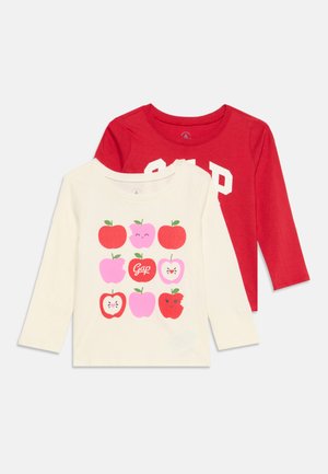 Deux chemises pour enfants à manches longues, une rouge avec un texte blanc "GAP", une crème avec neuf illustrations colorées de pommes, dont une avec un texte "Gap".