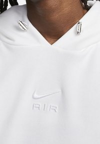 Witte hoodie met een V-hals, verstelbare zilverkleurige hardware en een reliëf "Nike AIR"-logo. Gemaakt van zacht materiaal met een gladde textuur.