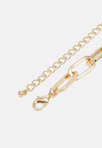 Bracelet en chaîne métallique dorée comprenant des maillons ovales, un fermoir homard et une finition texturée avec une apparence lisse et polie.