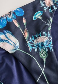 Patrón floral azul y blanco con tulipanes y cardos sobre tela morado oscuro, mostrando pétalos y tallos detallados.