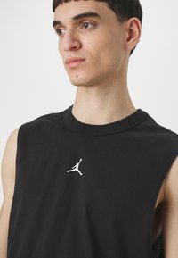 Černé bezrukávové tričko z bavlny s kulatým výstřihem a bílým logo Jordan na hrudi. Hladká textura s neformálním designem.