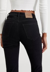 Mustat farkut slim fit -mallilla, joissa on kaksi takataskua ja ruskea nahkaletju vyötäröllä. Kangas on sileä.