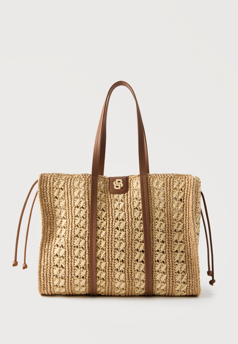 Sac cabas beige tissé avec motif tressé, anses en cuir marron, cordons latéraux et petit emblème doré au centre avant.