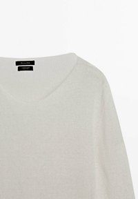 Pull en coton beige clair avec col en V, manches longues et un motif en maille texturée. L'étiquette est visible au niveau de l'encolure.
