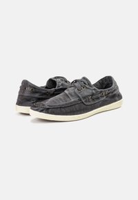 Čierne plátenné slip-on topánky s textúrovaným povrchom, ktoré majú mosadzné očká, biele gumové podrážky a zaoblený dizajn špičky.