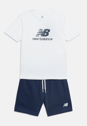 Λευκό κοντομάνικο μπλουζάκι με μαύρο λογότυπο New Balance, συνδυασμένο με σκούρο μπλε σορτς με κορδόνι και μικρό λευκό λογότυπο στο πόδι.