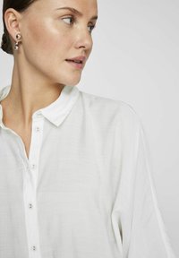 Camicia bianca con bottoni, realizzata in tessuto leggero, con colletto, superficie leggermente texture e vestibilità morbida.