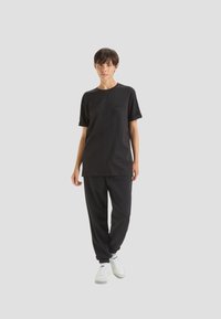 T-shirt nera in cotone con maniche corte e collo tondo, abbinata a pantaloni della tuta neri. Le sneakers presentano dettagli bianchi. Taglio semplice e rilassato.