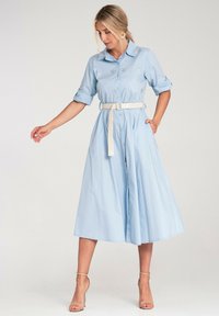 Jasnoniebieska sukienka koszulowa z krótkimi, podwiniętymi rękawami i ściąganym w talii fasonem, ozdobiona haftem kwiatowym oraz białym paskiem. Model sięgający do podłogi.