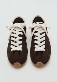 Zapatillas de ante marrón con cordones crema, puntera redondeada y suela de goma. La parte superior tiene una textura suave, con elementos de diseño mínimos.