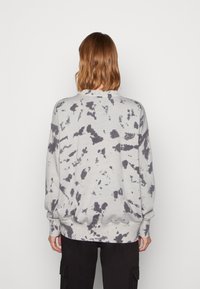 Sudadera gris de gran tamaño con un patrón tie-dye en gris más oscuro. Presenta puños y dobladillo acanalados, y un cuello redondo. Textura de tela suave.