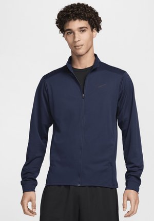 Marineblå zip-jakke med lange ærmer, lavet af glat stof. Forskellige skulderpaneler og en sort Nike-logo på venstre bryst.