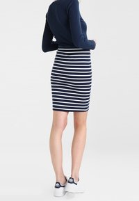 Mörkblå långärmad topp i kombination med en figurnära randig pennkjol med horisontella vita ränder och vita sneakers.