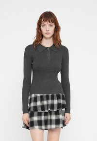 Grå ribbet strikket topp med kragehals og tre-knapp foran, kombinert med et svart-og-hvitt rutete, lagdelt skjørt.