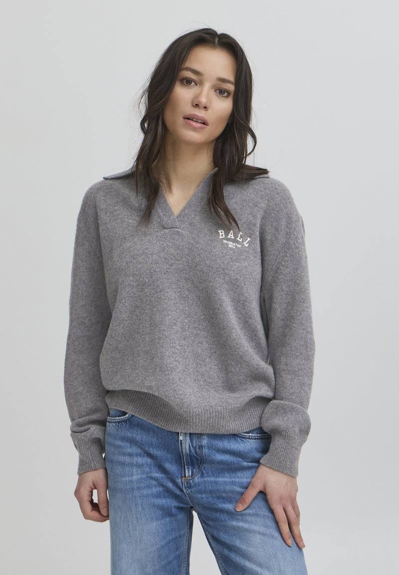 Gray knit sweater with a V-neck, ribbed cuffs, and a logo that reads "BALI" on the left chest. Paired with light blue jeans.