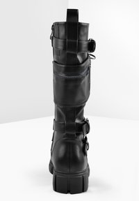 Bota alta de cuero negro hasta la rodilla con punta redonda, suela de goma gruesa, hebillas decorativas, cremallera lateral y paneles texturizados.