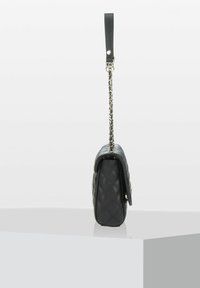 Sac à main en cuir noir matelassé avec une silhouette plate, doté d'une sangle en cuir noir et d'une quincaillerie en chaîne argentée. La vue latérale met en avant sa forme compacte.