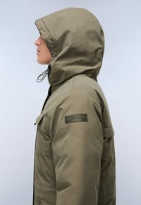 Giacca a vento khaki con cappuccio, zip, coulisse e tasche laterali. Presenta un tessuto testurizzato e una patch del marchio sulla manica.