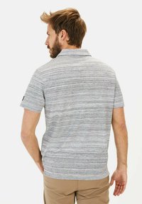 Gråstribet polo-shirt med krave og korte ærmer, lavet af et struktureret stof. Modellen har ryggen til.
