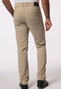 Beżowe spodnie bawełniane z prostymi nogawkami, z dwoma tylnymi kieszeniami i brązowym skórzanym akcentem przy pasie.