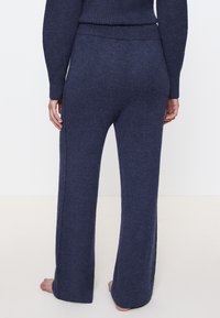 Granatowe, dzianinowe spodnie o szerokich nogawkach z miękką fakturą, z wysokim stanem i subtelnymi bocznymi szwami. Fason jest luźny i wygodny.