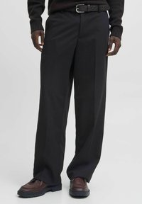 Czarne, szerokie spodnie z gładkiego materiału, z wysokim stanem i plisami z przodu. Połączone z brązowymi skórzanymi butami i pasującym paskiem.