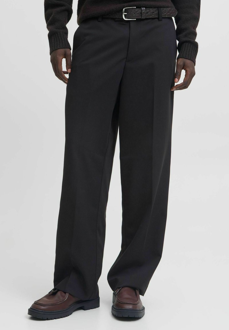 Czarne, szerokie spodnie z gładkiego materiału, z wysokim stanem i plisami z przodu. Połączone z brązowymi skórzanymi butami i pasującym paskiem.