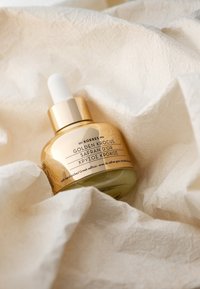 Gyllene glasdropperflaska med ett guldlock, märkt "Golden Krocus Safran d'Or." Ligger på texturerad krämfärgad tyg.