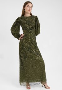 Oliven grøn glitter maxi kjole med lange pufærmer, detaljeret perlesyningsmønster og tætsiddende talje, prydet med gennemsigtige detaljer ved kanten.