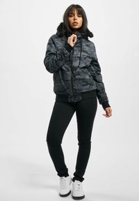Kamouflagejakke med krave af sort kunstpels, lynlås lukning og ribbede manchetter. Båret med sorte bukser og hvide sneakers.